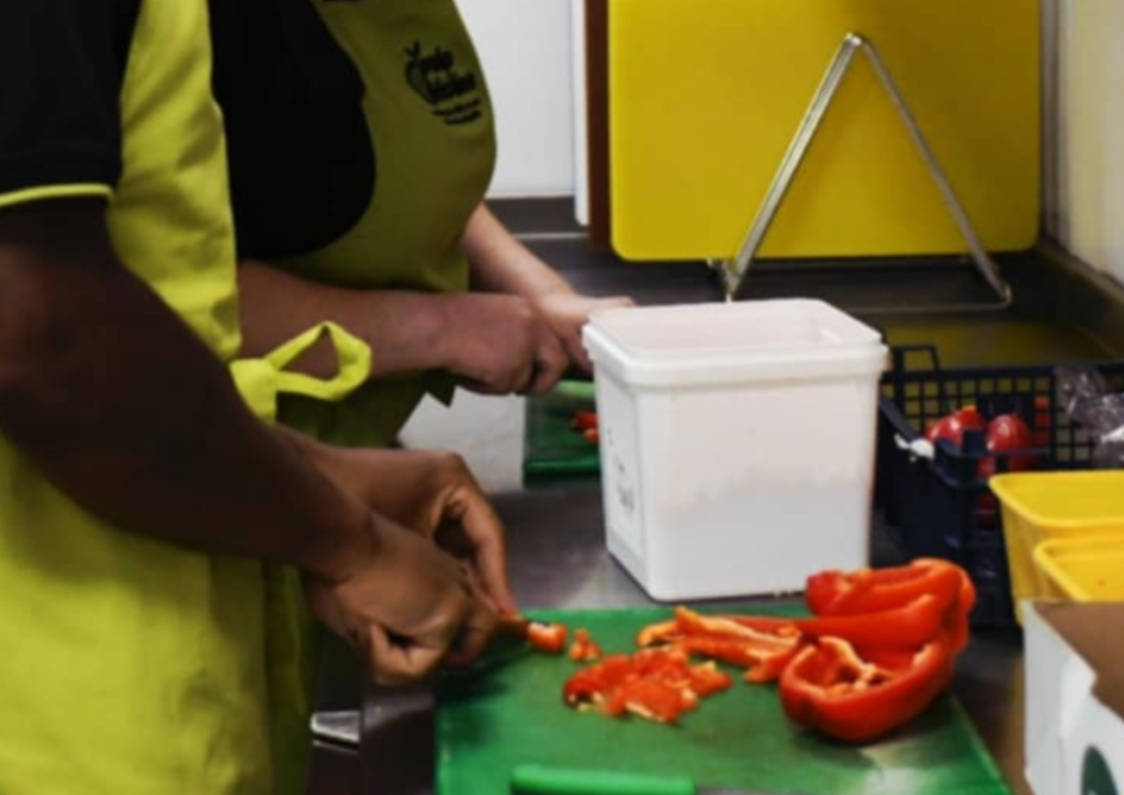 catering assistant cooking in a kitchen. image shows people chopping a red pepper