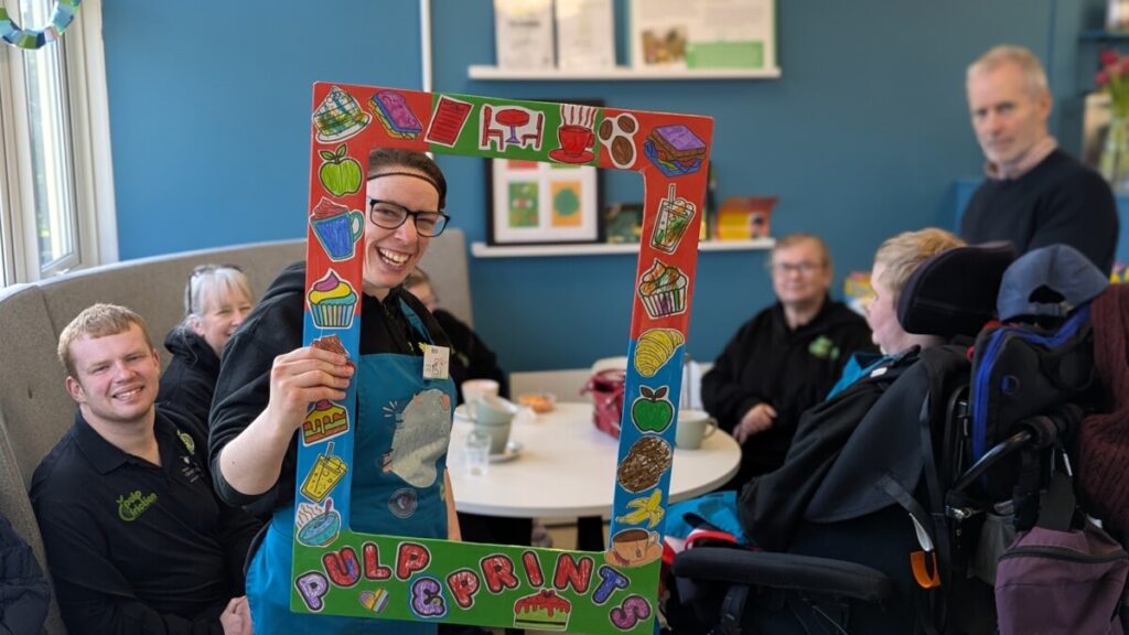 Pulp Friction Members holding a 'Pulp & Prints' frame and smiling
